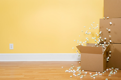 Packing Peanuts flying out of an open carboard box, with unopened boxes stacked against the wall inside of a home.