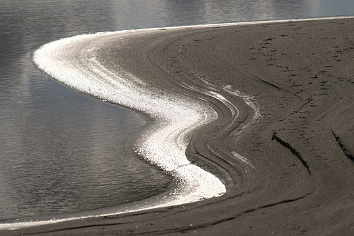 Abstract view of the coastal edge of sand and water in backlit sunlight