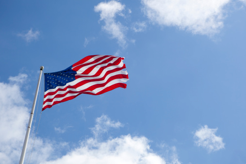 A large American flag blows in the wind against a bright blue sky.