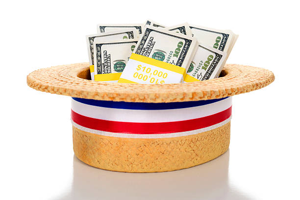 Political Fund raising Political fund raising / contributions. A Patriotic skimmer hat sits full of bundles of $100 bills with reflection on a white background rnc convention stock pictures, royalty-free photos & images