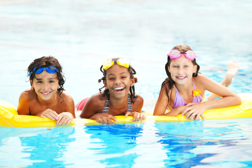 Smiling children wearing snorkel goggles and floating on a yellow raft.