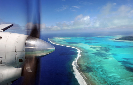 A turbo prop aircraft crosses a turquoise lagoon in the South Pacific