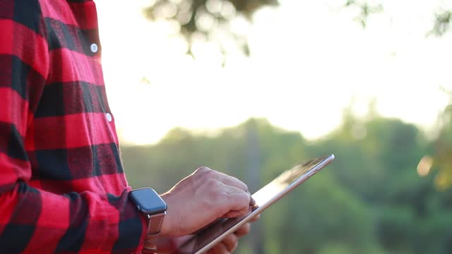 Farmer wearing plaid shirt, sunset background Use tablets for internet-based planning and control, smart farms, data collection and transmission.