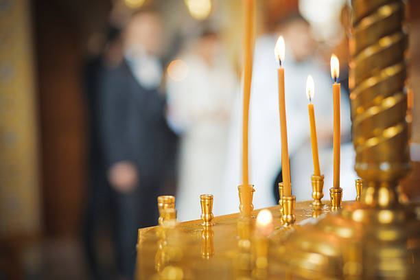 Burning candles in a Russian ortodox church. Close-up of ordinary church interior. Selective focus. With wedding ceremony on background.