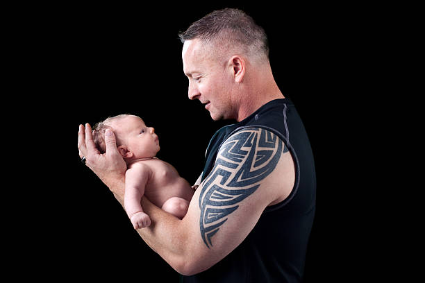 отец держит ребенка на черном фоне - muscular build men tattoo human arm стоковые фото и изображения