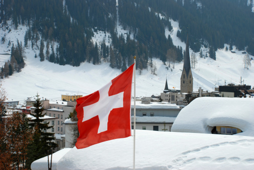 Swiss flag in Davos town with church and mountains in the background. Davos is a ski resort and location of the annual World Economic Forum.Please see more flag pictures: