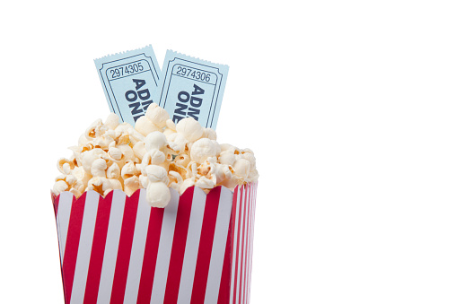 Red Striped Popcorn Bag And Movie Ticket On White Background For Cinema Concept.Two blue theatre tickets are placed on top of popcorn bag.The photo was shot in studio with a full frame DSLR camera and a macro lens.no people in frame. 