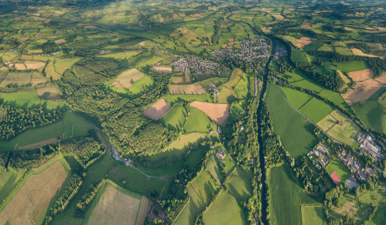 Green summer pasture and patchwork fields around a quiet country town beside a meandering river from high in a hot air balloon. ProPhoto RGB profile for maximum color fidelity and gamut.