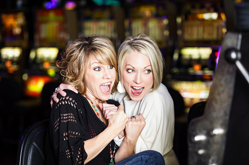 Two excited smiling women winning at a slot machine inside a casino.
