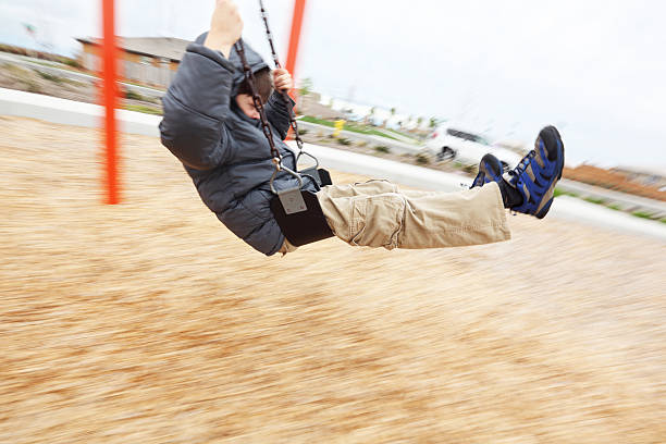 Boy on Swing Elementary age boy having fun on a swing in park on a cold day. Motion Blur. mm1 stock pictures, royalty-free photos & images
