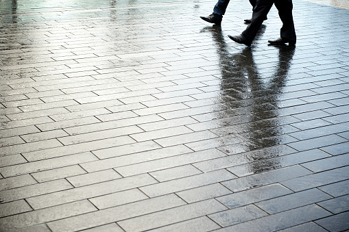 Pair of businessmen walking together with shadows reflecting on smooth wet pavement