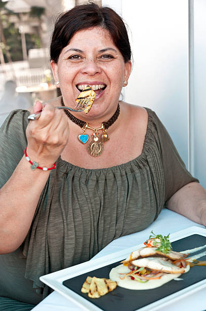Hispanic mature woman having lunch holding a fork while eating smiling