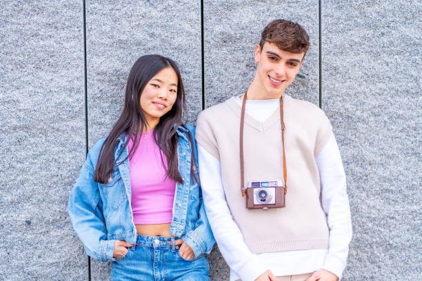 Multi-ethnic young couple leaning on a wall carrying a camera