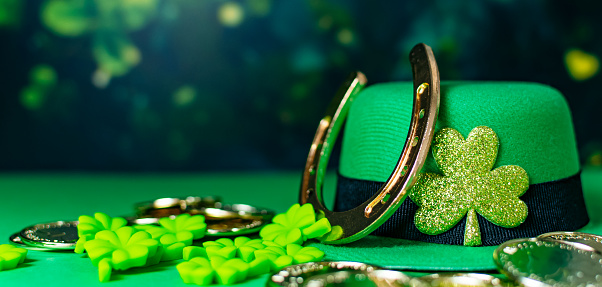 Happy St Patrick Day leprechaun hat with gold coins and lucky charms on green background.