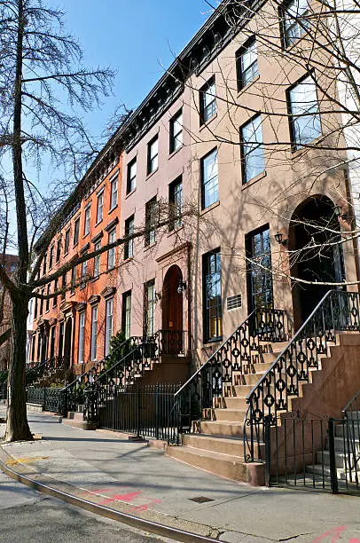 "A historic row of Greek or Renaissance Revival style brownstone and brick row houses are seen along St. Luke's Place in the West Greenwich Village neighborhood of Manhattan, New York City. The homes were built in 1852-1853 by wealthy city merchants, prominent political figures or up and coming immigrant families. The facades are mostly the original design as well as the iron railings at the front stoops and doorway entrances. The street is an example of historic New York mostly as it was over 160 years ago."