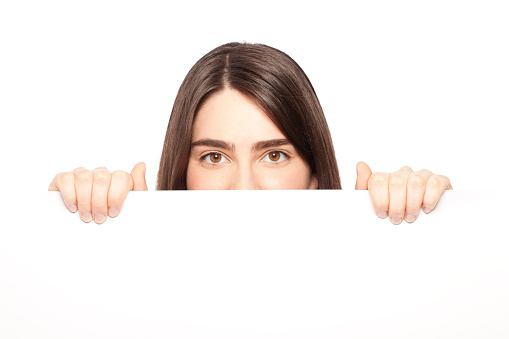Young woman peeking behind blank sheet
