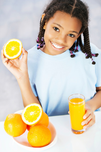 Little girl making juice. Holding Orange and looking at the camera.