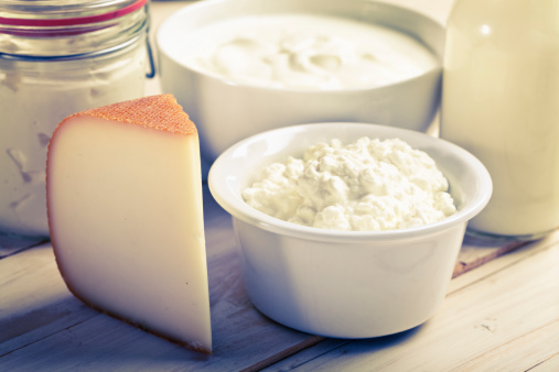 dairy products such as cheese, yoghurt, cottage cheese, milk in a glass bottle on wooden table, image is crossprocessed