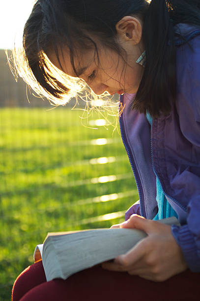 istock School Girl Sits Reading Book in Sunny Park 185249213