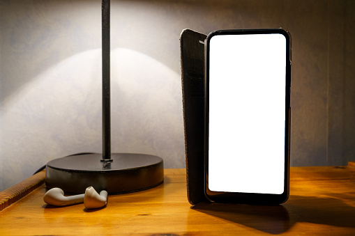 Smart phone with flip case and empty white screen on bedside table, clipping path