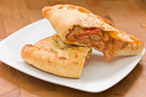 A high angle shot of a white plate with a calzone cut in half revealing the delicacies inside. Shot on a wooden  background.