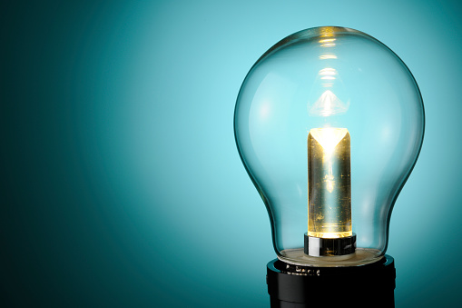 Close-up of illuminated LED light bulb against blue background with copy space.