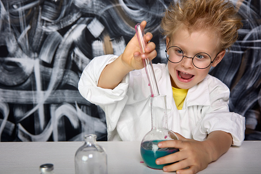 Smart boy in glasses and white coat conducts chemical experiments in laboratory