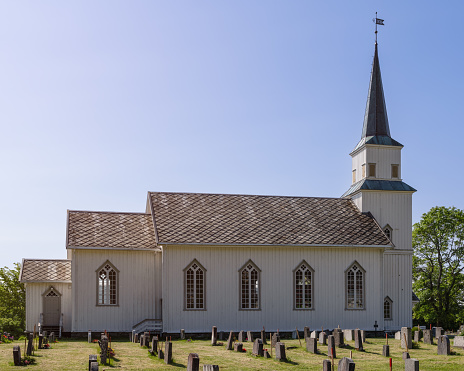 A warm summer sun illuminates the wooden Kvam Church in Nord-Fron, Norway, surrounded by a well-maintained cemetery with grave markers