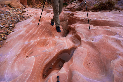 View of Hiker Hiking Slot Canyon in Desert Southwest USA - Red rock canyon and smooth sandstone rock features with view of hiker cropped from waist down.