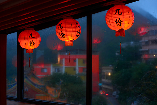 Sunset scene in the rain of Jiufen in a tea room, Taipei, Taiwan.The weather is cloudy with blue color. The Chinese on the lanterns means “Jiufen” with Chinese character. There are sea and Chinese temple on the blur background. Good photos for travel use.