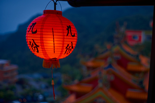 Sunset scene in the rain of Jiufen in a tea room, Taipei, Taiwan.The weather is cloudy with blue color. The Chinese on the lanterns means “Jiufen” with Chinese character. There are sea and Chinese temple on the blur background. Good photos for travel use.