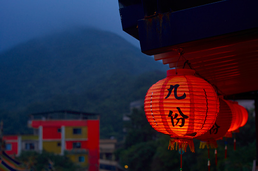 Sunset scene in the rain of Jiufen in a tea room, Taipei, Taiwan.The weather is cloudy with blue color. The Chinese on the lanterns means “Jiufen” with Chinese character. There are sea and Chinese temple on the blur background. Good photos for travel use.