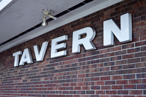 Old raised white tavern sign on a brick wall.