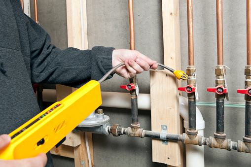 A worker is using a leak detector near a set of house gas lines at a renovation site. Very small gas leaks are often found at pipe joints in older construction.