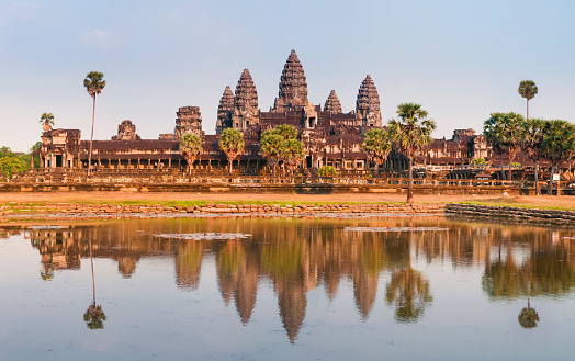 A panoramic view of the spectacular ruins of the Angkor Wat temple complex in Cambodia.  Taken in golden evening light just before sunset, the scene is reflected in the large lotus pond in front.