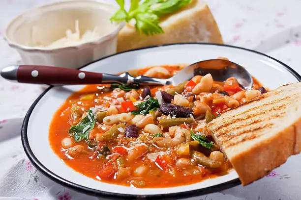 Close-up of minestrone soup in an enamel plate with bread and parmesan.