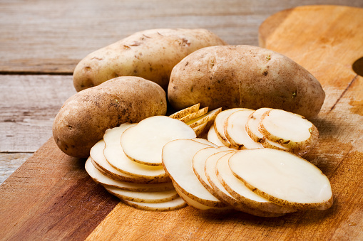 Whole and sliced russet potatoes on an old wood cutting board.