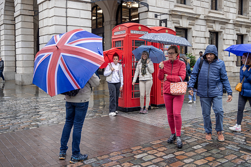 Covent Garden, London, England - October 29th 2023:  Man with a Union Jack umbrella in front of a red telephone boot on a rainy day