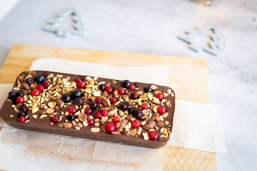 Delicious homemade chocolate Christmas cake with nuts and berries on the top. Fresh gingerbread or dark cake with cocoa. Chocolate fudge brownies with Christmas decorations in background.