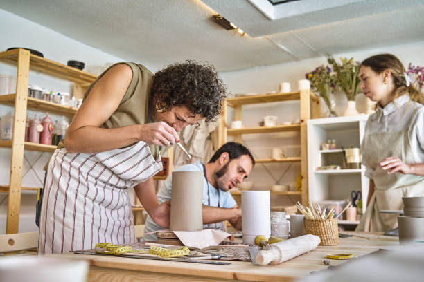 Artisans crafting pottery in a sunny workshop Focused artisans with aprons handcraft pottery amidst a bright, organized ceramics studio with tools homemade pottery wheel stock pictures, royalty-free photos & images