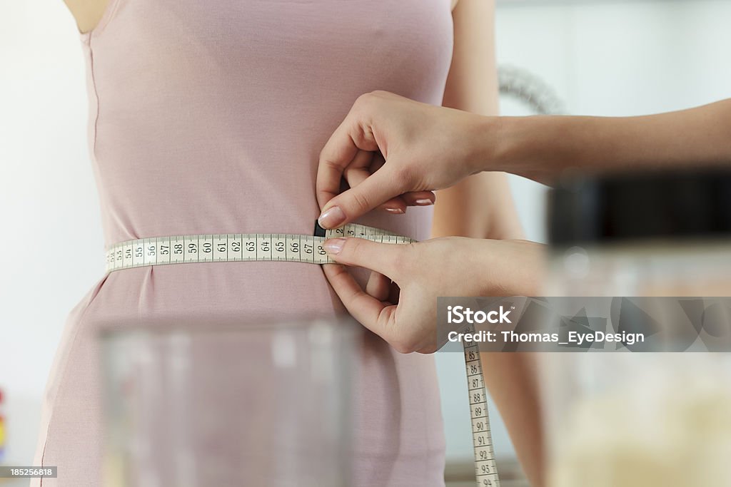 Woman Measuring Friend's Waist "Close-up of two women on a diet, tracking they weight loss program. One of the women is measuring her friend's waist with a tape measure. Horizontal shot." 25-29 Years Stock Photo