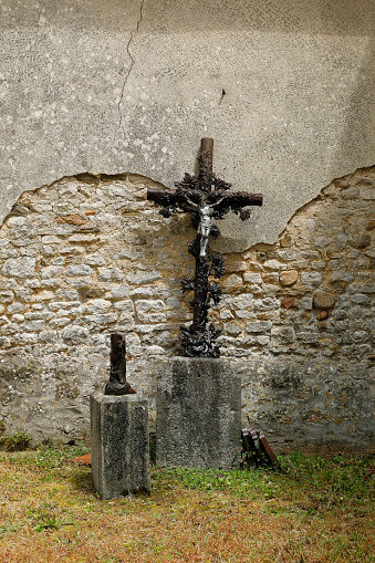 Broken cross with the crucified Jesus leaning against a church wall