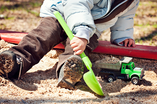 Closeup of little boy sitting in the sandbox and playing with toy truck and shovel.Similar: