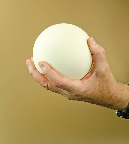A senior's hand holding a white sphere as a symbol of hope. Tan background with copy space on the sphere. Gripped