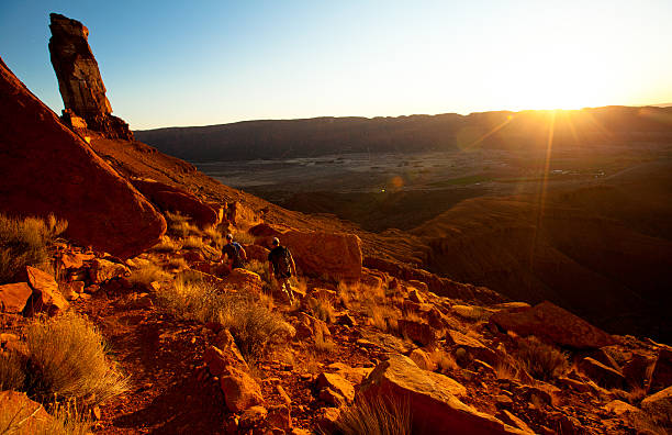 Two hikers walking through the red dirt of the desert near Moab Utah at sunset.