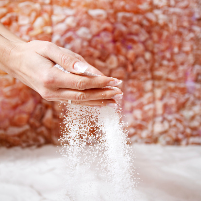 Woman pouring salt out of her hands while getting halotherapy treatment in salt room.