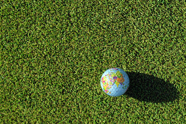 Golf ball on a tee on grass, with a golf club and the reflection of a world globe on the golf ball.