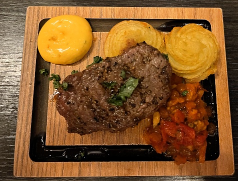 Steak accompanied by mashed potatoes, tomatoes and sauce all resting on a cutting board
