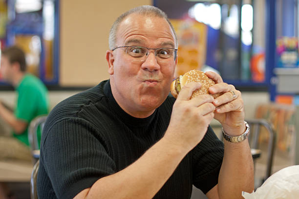 man eating burger in fast food restaurant stock photo