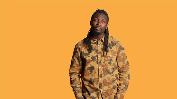 Shocked african american man saying wow on camera feeling amazed by something in front of him. Surprised excited person with dreads smiling in studio over orange background.